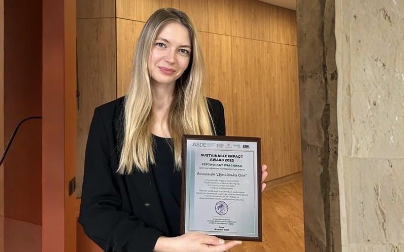 A woman holding a framed certificate for the Sustainable Impact Awards Ukraine 2025, standing in an indoor setting.